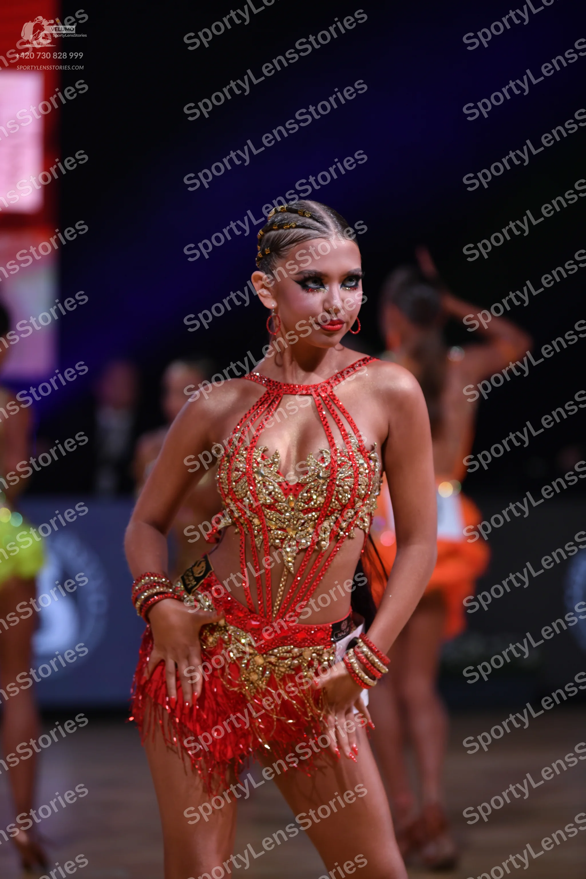 Dancesport competitor: Female dancer (foreground): red Latin dress with gold sequin embellishments, a c