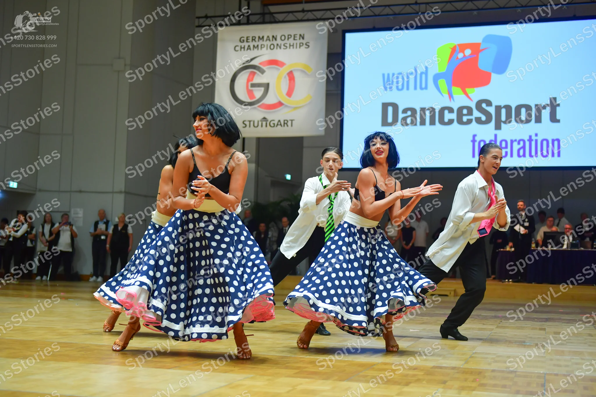 Dancesport competitor: Female dancers: black camisole tops and large, flared navy blue skirts with whit