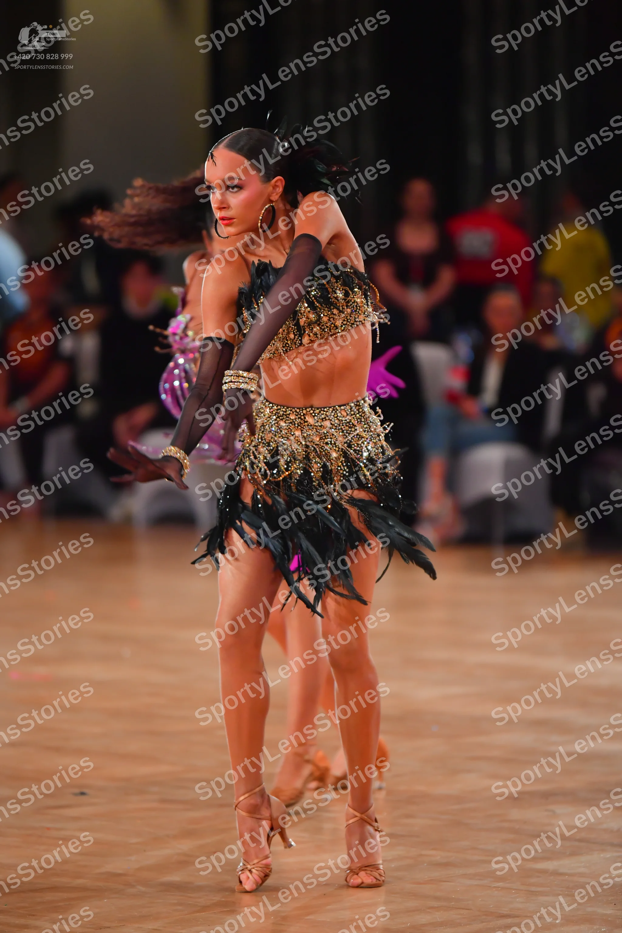 Dancesport competitor: Female dancer in foreground: black and gold sequin Latin dance costume with a cr
