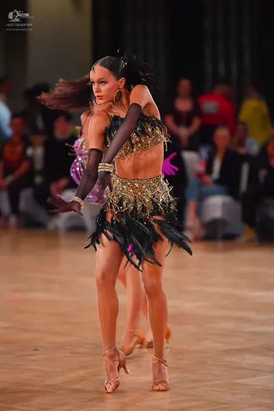 Dancesport competitor: Female dancer in foreground: black and gold sequin Latin dance costume with a cr