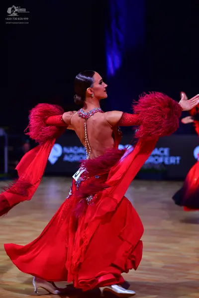 Dancesport competitor: Female dancer: red Latin dress with large red feather decorations on the sleeves