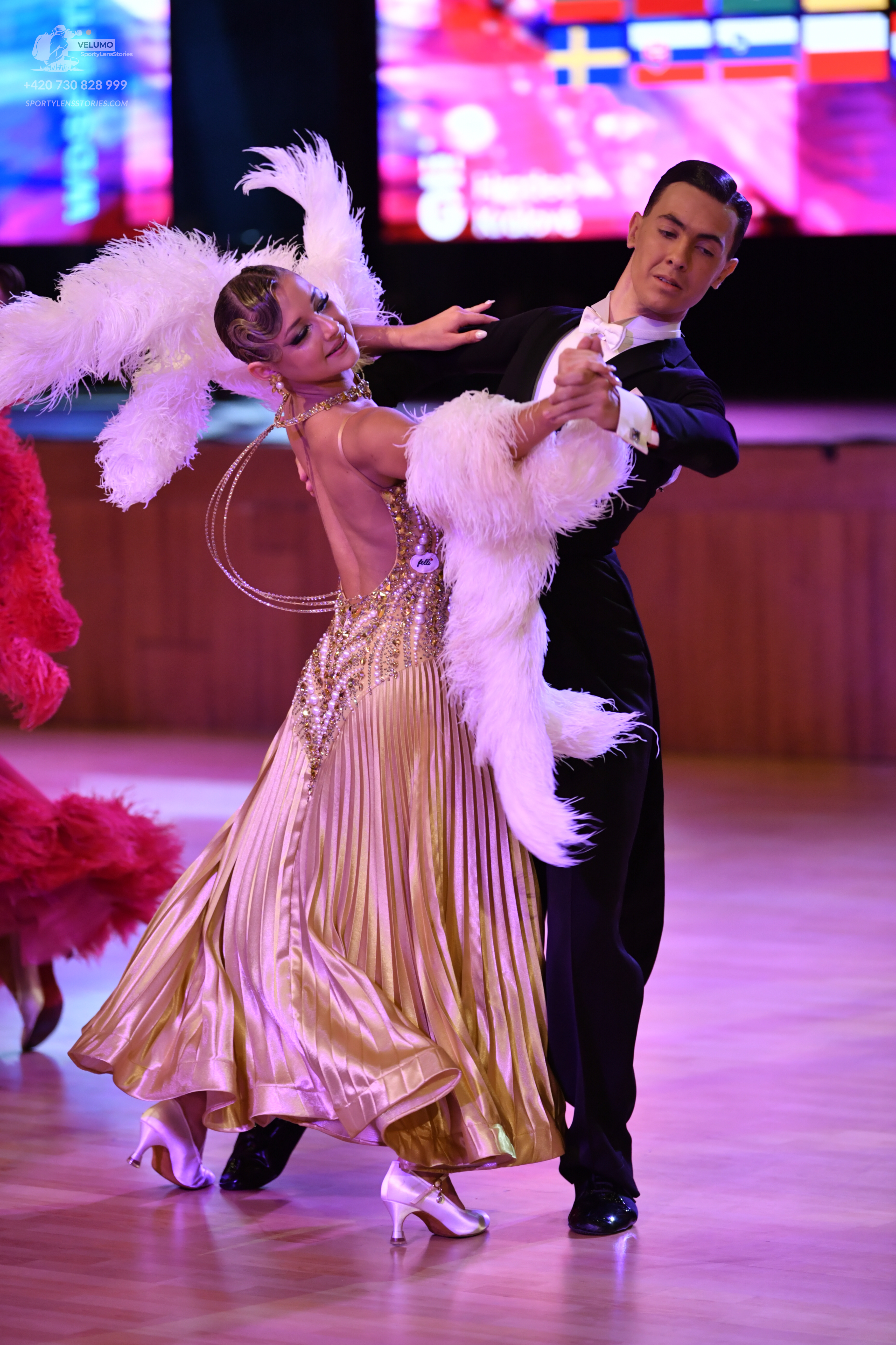 Dancesport competitor: Female dancer: gold pleated ballroom dress with a sequin-embellished bodice and 