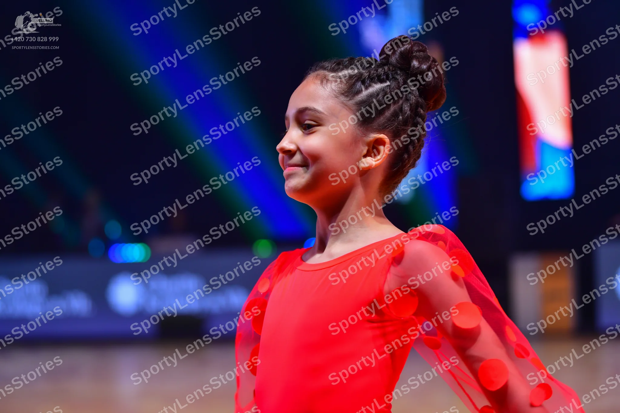Dancesport competitor: Female dancer: red latin dress with sheer sleeves featuring red circular embelli