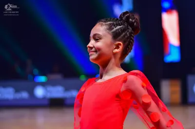 Dancesport competitor: Female dancer: red latin dress with sheer sleeves featuring red circular embelli