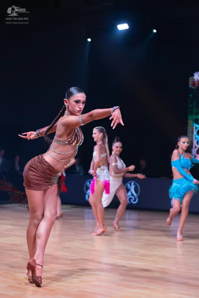 Dancesport competitor: Female dancer in foreground: bronze/brown sequined latin dress with thin straps 