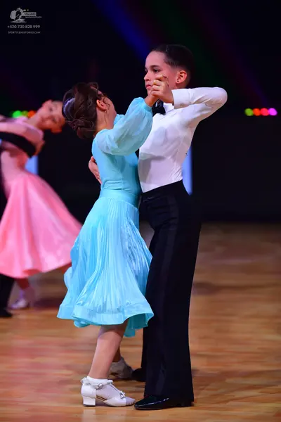 Dancesport competitor: Female dancer (foreground): light blue long-sleeved dress with a pleated skirt; 