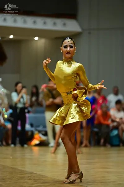 Dancesport competitor: Female dancer: metallic gold long-sleeved, high-neck latin dress with a short fl