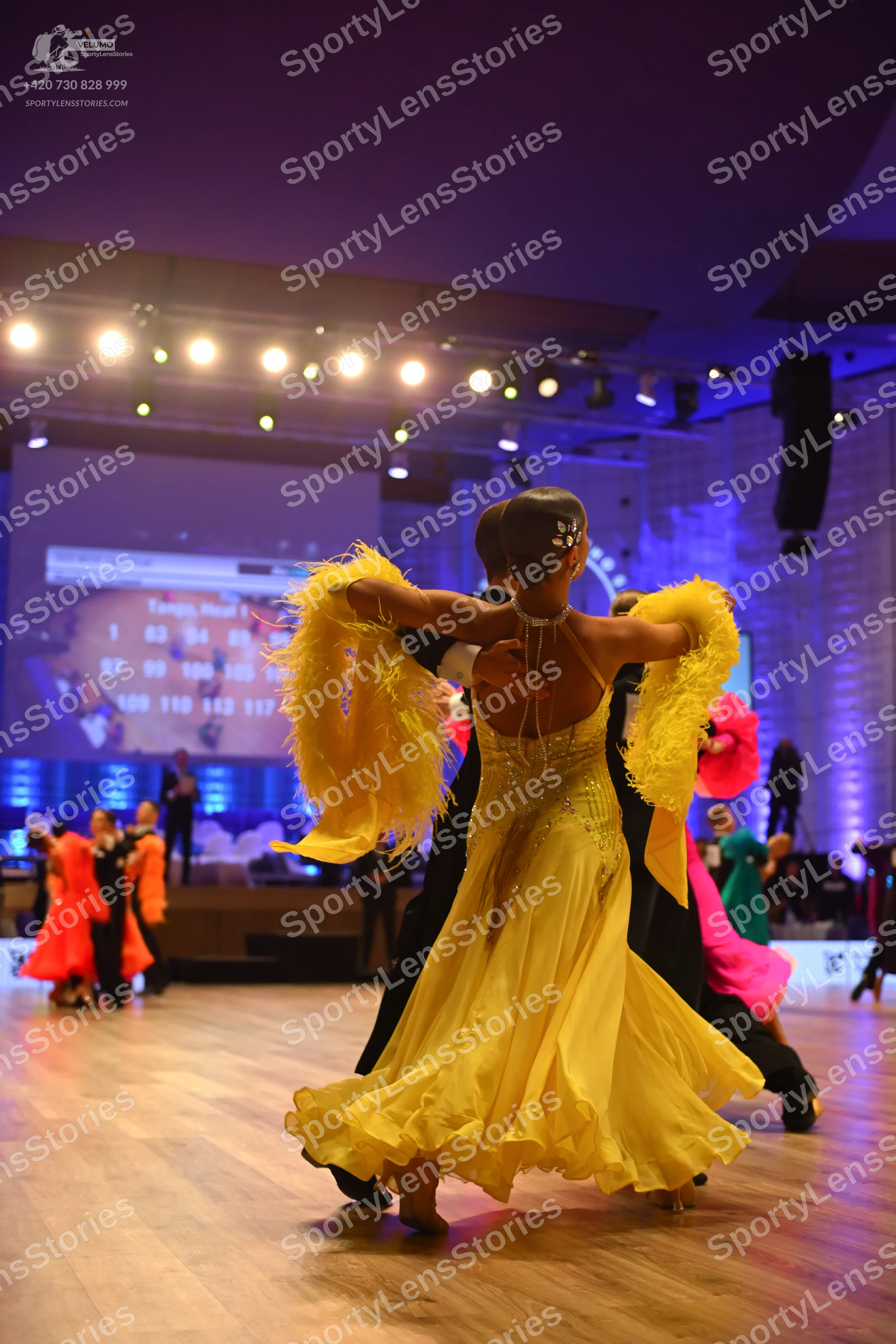 Dancesport competitor: Female dancer in foreground: yellow latin dress with a backless bodice and a vol