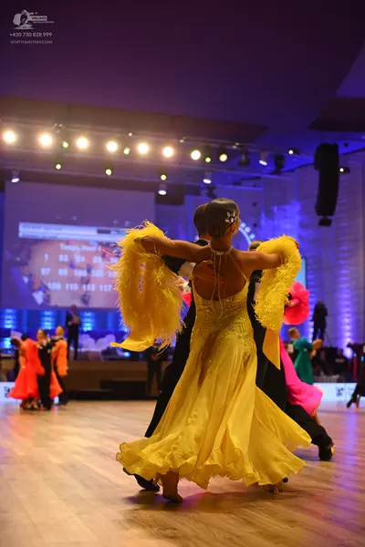 Dancesport competitor: Female dancer in foreground: yellow latin dress with a backless bodice and a vol