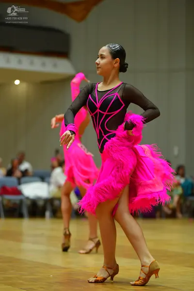 Dancesport competitor: Female dancer 1: black long-sleeved latin dress with bright pink mesh detailing 