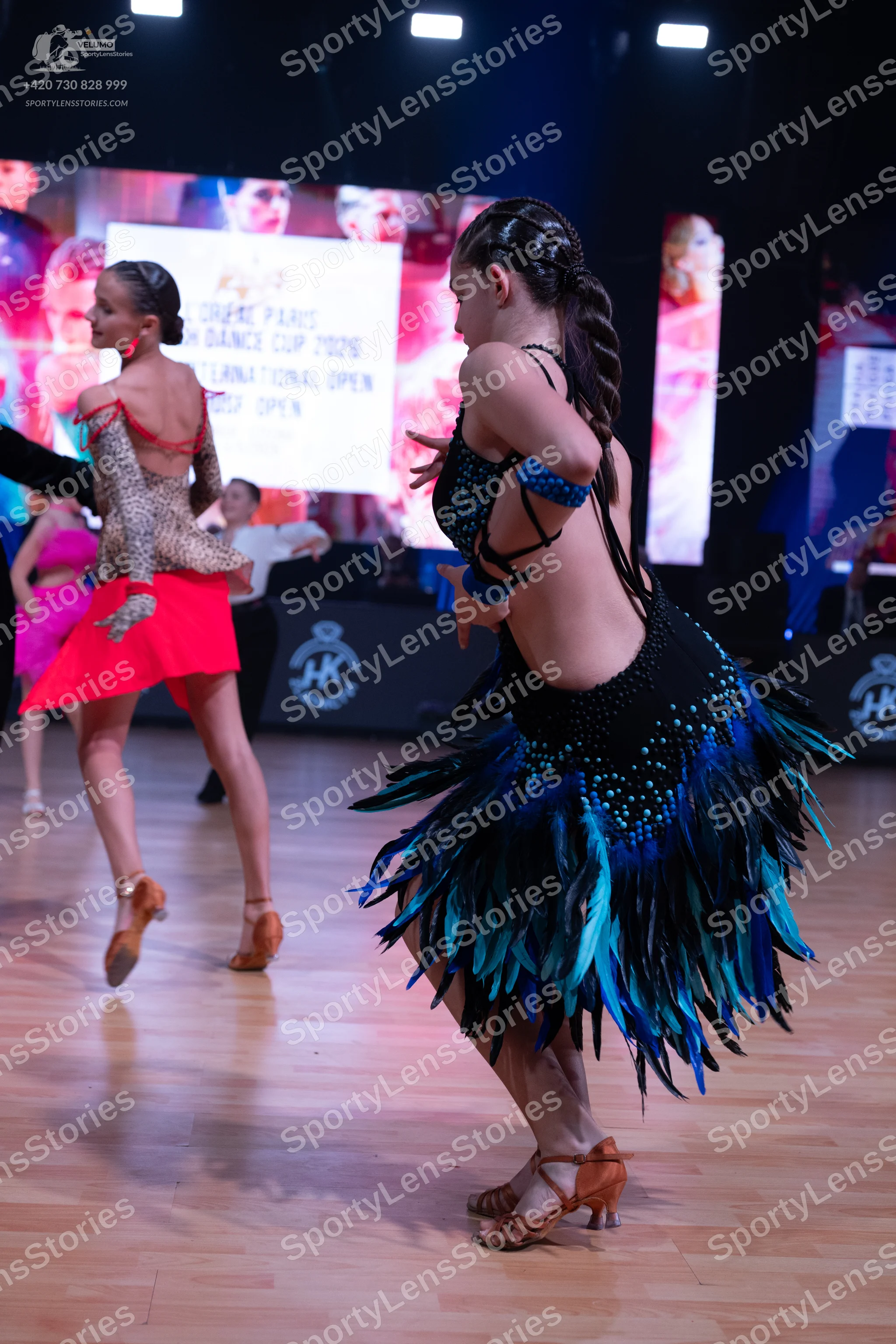 Dancesport competitor: Female dancer (foreground): black Latin dance dress with blue and teal sequins a