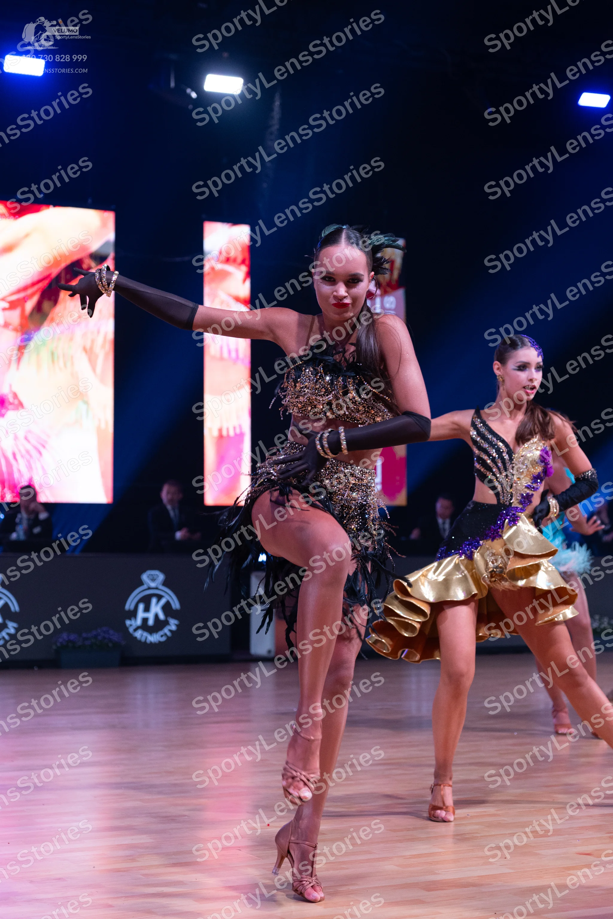 Dancesport competitor: Female dancer 1: dark Latin dance dress with gold sequins and long black fringe,