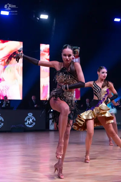 Dancesport competitor: Female dancer 1: dark Latin dance dress with gold sequins and long black fringe,