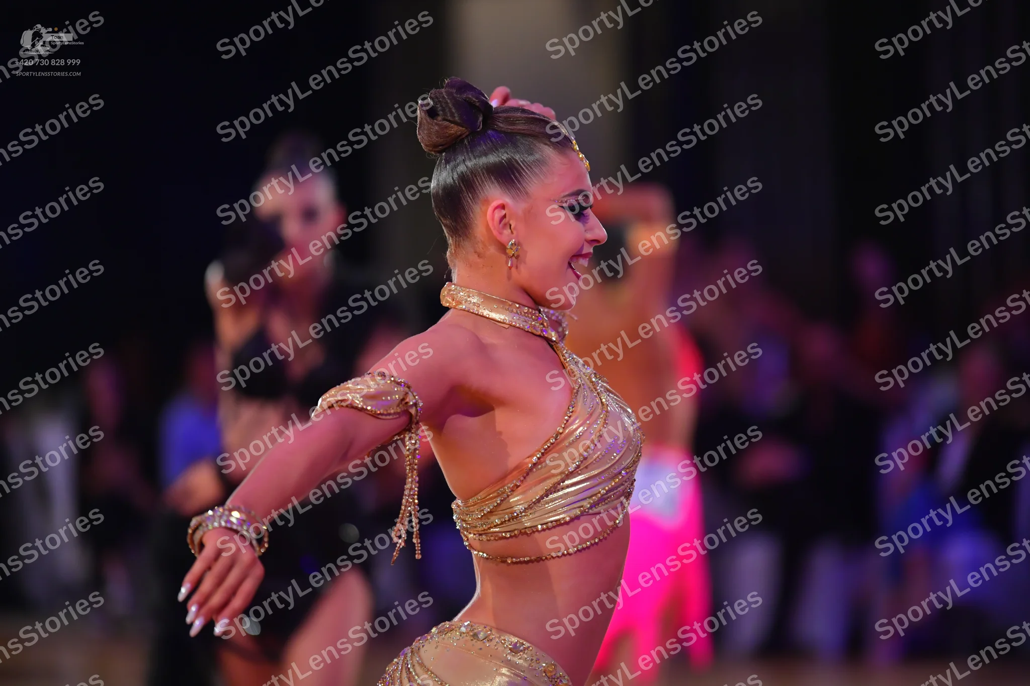 Dancesport competitor: Female dancer in foreground: gold metallic Latin dance costume consisting of a c