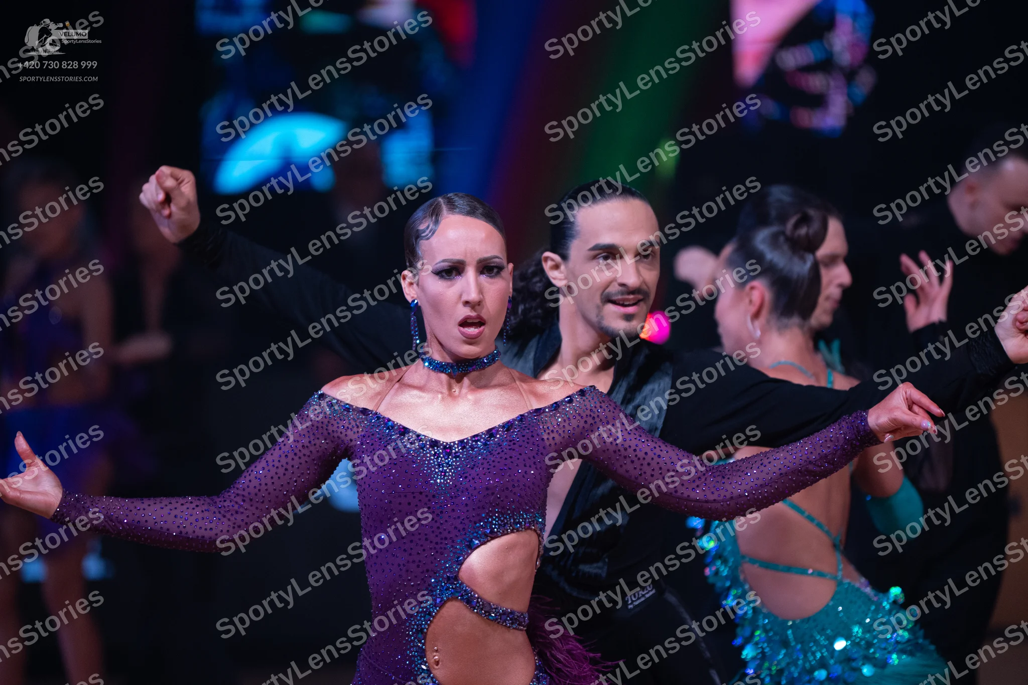 Dancesport competitor: Female dancer in foreground: purple sequined Latin dress with long sleeves and w