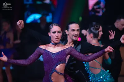 Dancesport competitor: Female dancer in foreground: purple sequined Latin dress with long sleeves and w