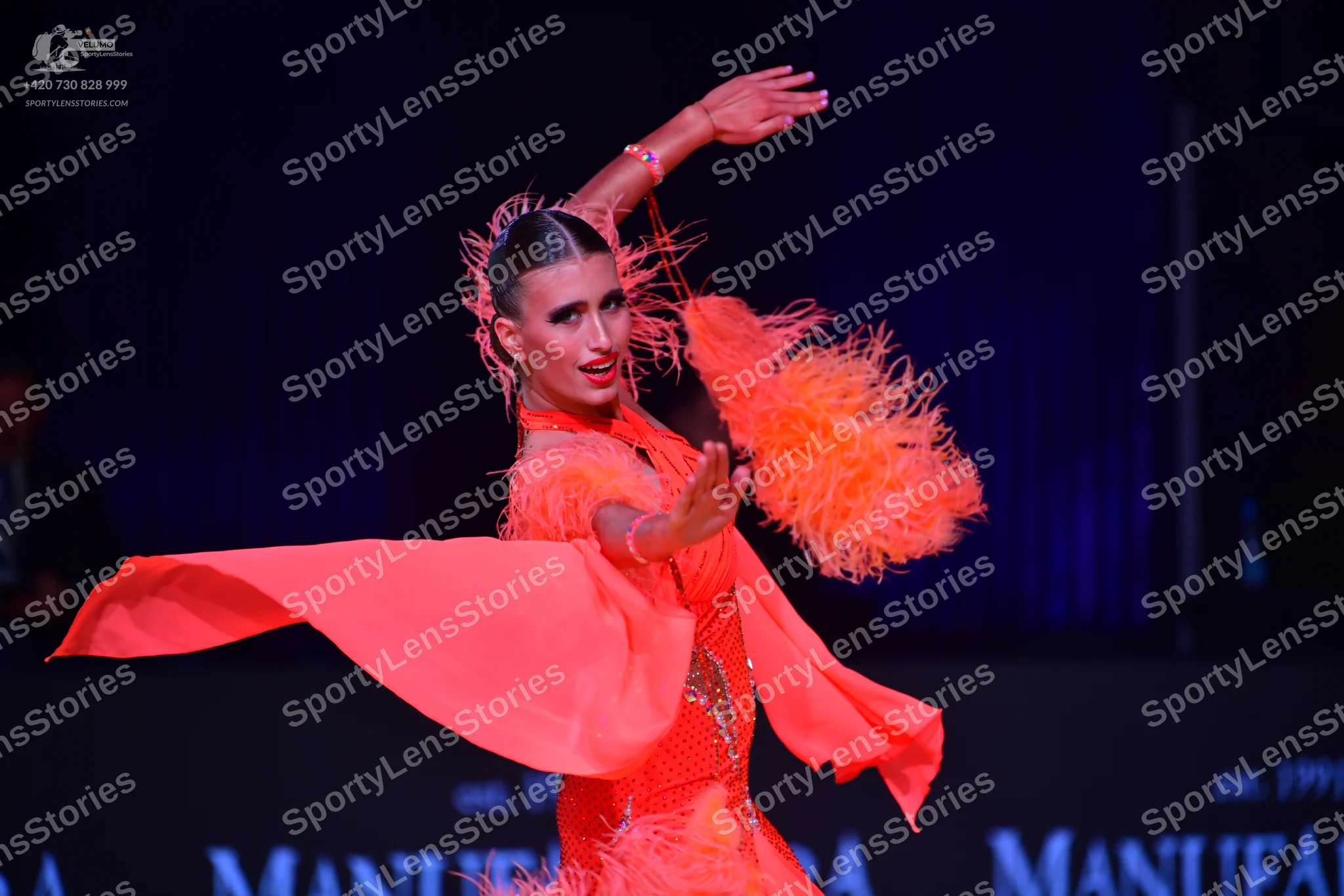 Dancesport competitor: Female dancer: bright orange Latin dance dress with feather accents on the sleev