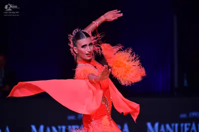 Dancesport competitor: Female dancer: bright orange Latin dance dress with feather accents on the sleev