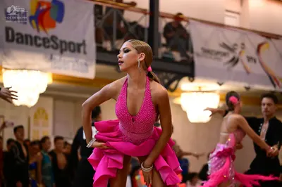 Dancesport competitor: Main female dancer: bright pink sequined Latin dress with a ruffled skirt and de