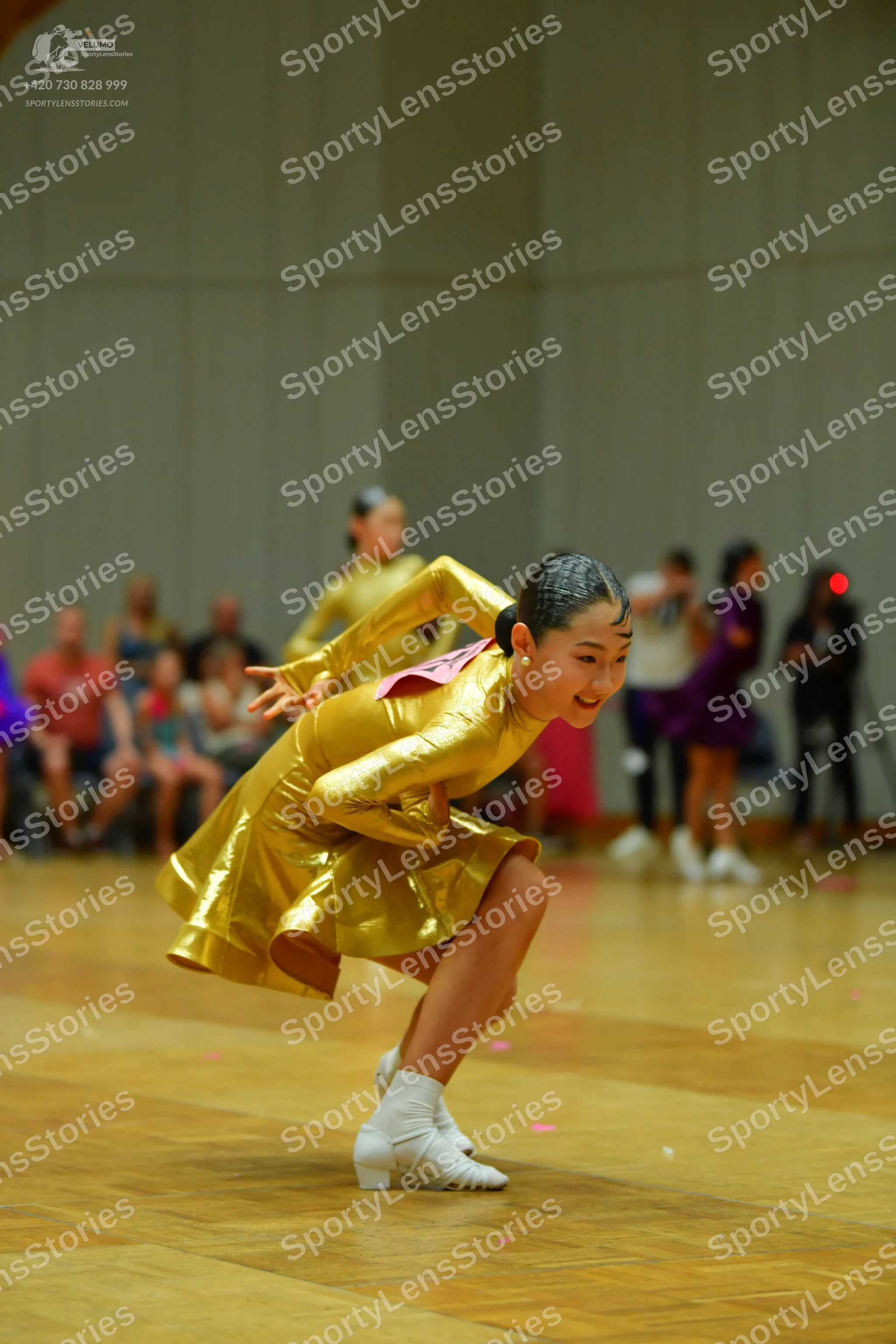 Dancesport competitor: Female dancer in foreground: gold metallic long-sleeved dress with a flared skir