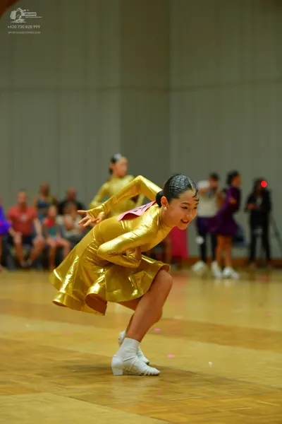 Dancesport competitor: Female dancer in foreground: gold metallic long-sleeved dress with a flared skir