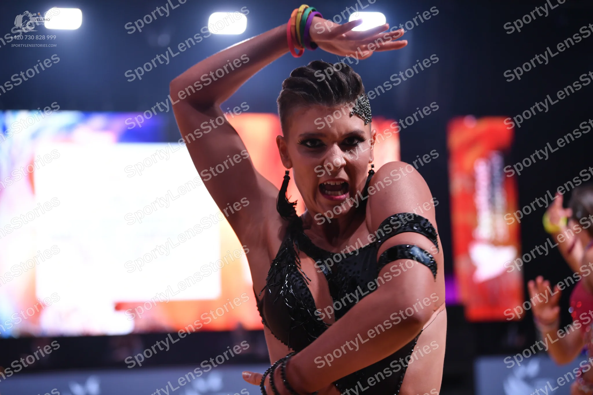Dancesport competitor: Female dancer in foreground: black Latin dance costume with sequins on the bodic