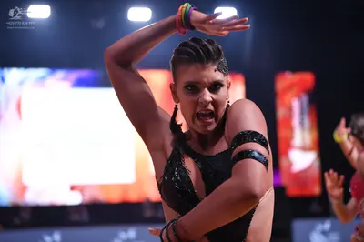 Dancesport competitor: Female dancer in foreground: black Latin dance costume with sequins on the bodic