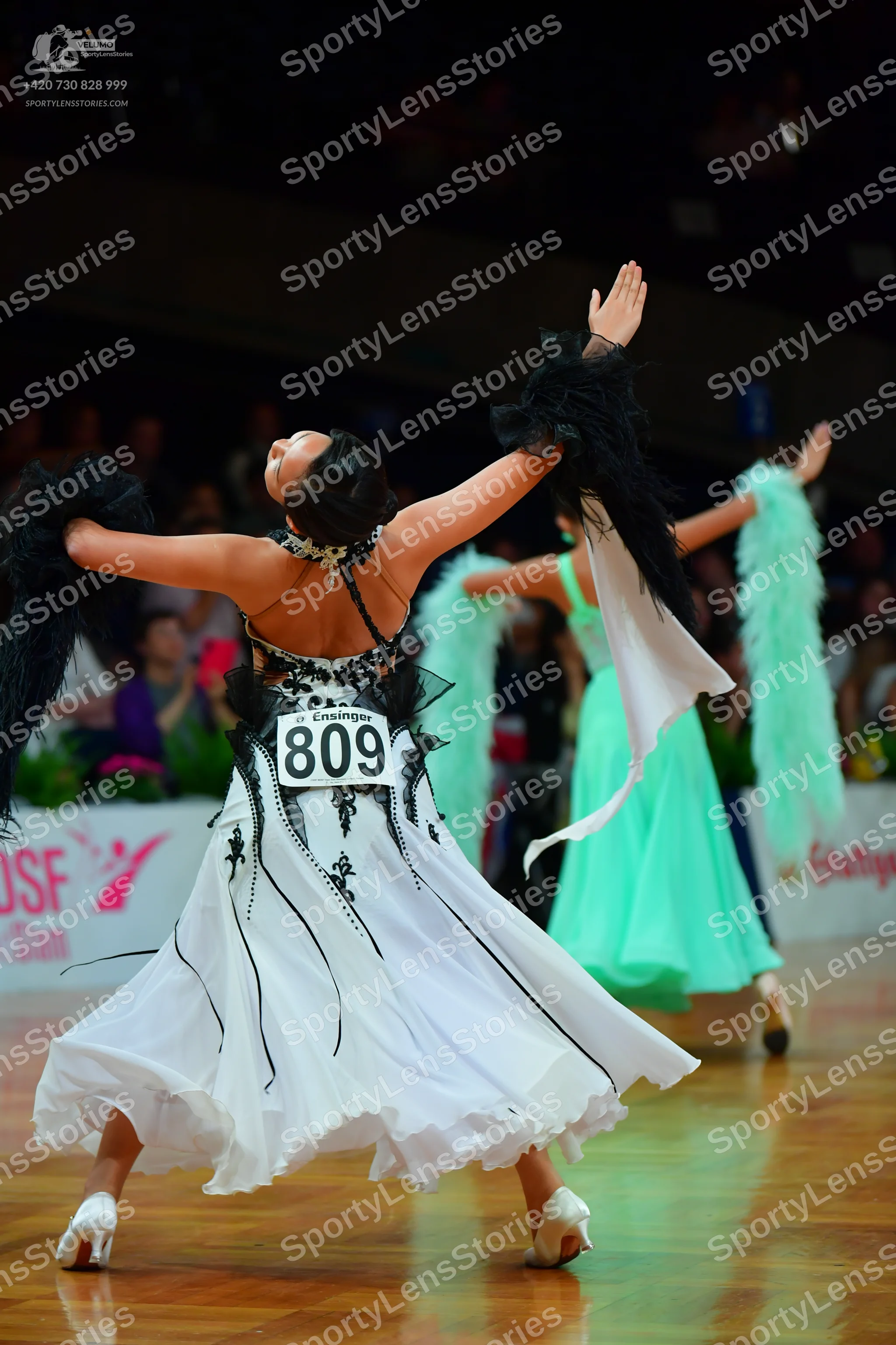 Dancesport competitor: Female dancer in foreground: white ballgown with black lace-like trim and black 