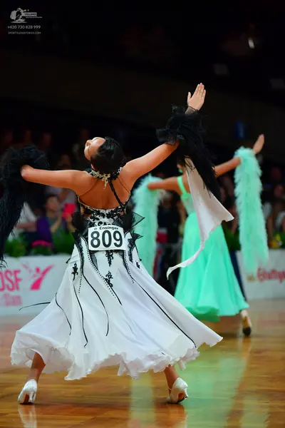 Dancesport competitor: Female dancer in foreground: white ballgown with black lace-like trim and black 