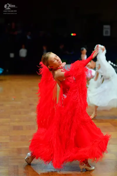 Dancesport competitor: Female dancer in foreground: red ballroom dress with long, flowing red fringe on