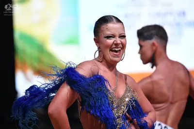 Dancesport competitor: Female dancer: royal blue and gold latin dress with large blue feather accents o
