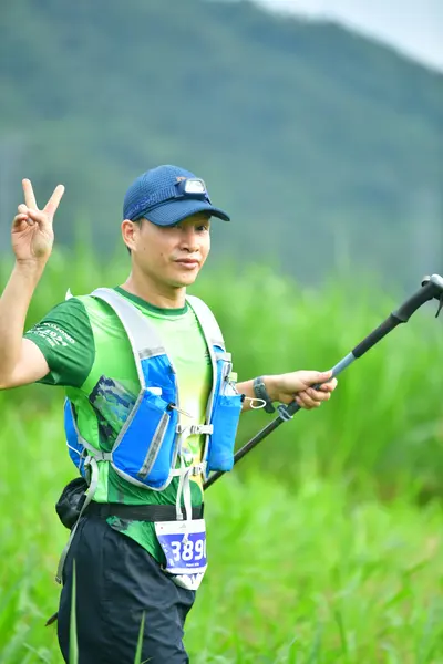 Marathon runner #389: Runner 1: green jersey, black shorts, blue and white hydration vest, blue cap, b