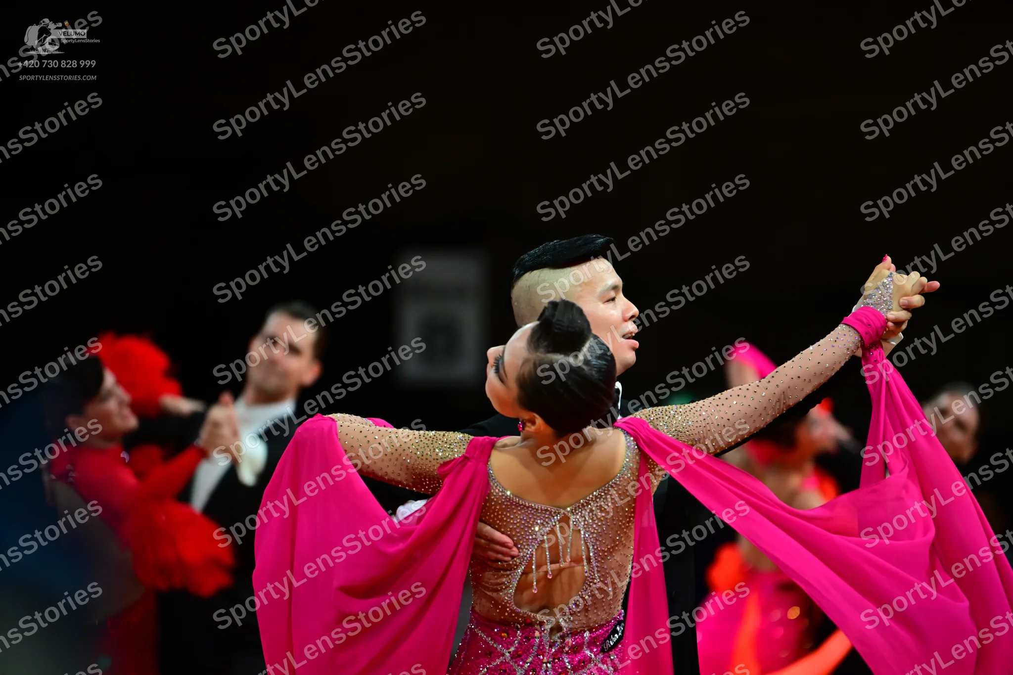 Dancesport competitor: Foreground female dancer: bright pink latin dress with sheer, rhinestone-embelli