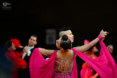 Dancesport competitor: Foreground female dancer: bright pink latin dress with sheer, rhinestone-embelli
