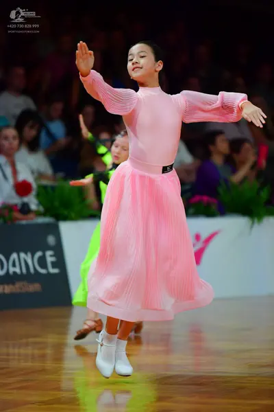Dancesport competitor: Female dancer: pink long-sleeved dress with pleated sleeves and skirt, and a bla