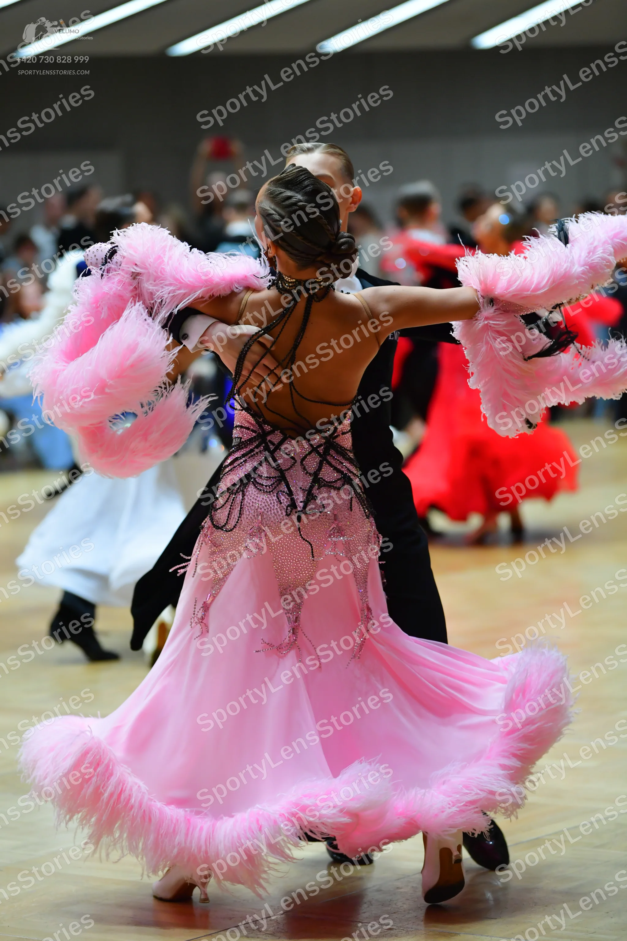 Dancesport competitor: Female dancer in foreground: pink dress with large pink feathers on the sleeves