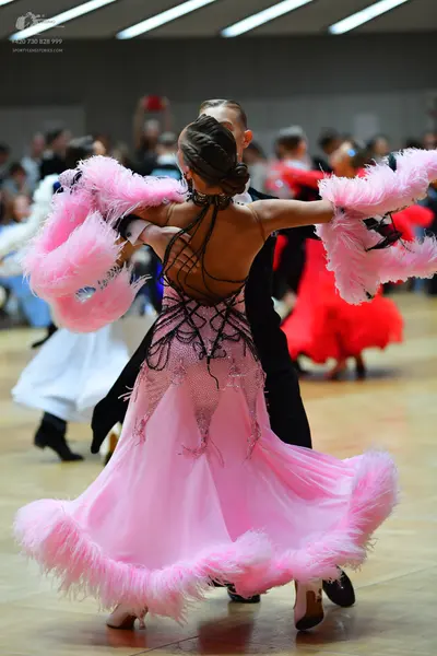 Dancesport competitor: Female dancer in foreground: pink dress with large pink feathers on the sleeves 