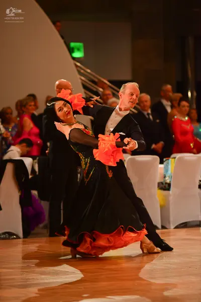 Dancesport competitor: Female dancer: black ballgown with large orange/peach ruffles at the hem and nec