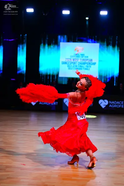 Dancesport competitor: Female dancer: red latin dress with large red feather attachments on the arms an
