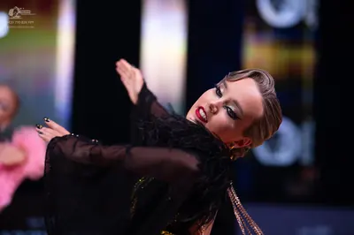 Dancesport competitor: Female dancer: black long-sleeved sheer top with black feather detailing and gol