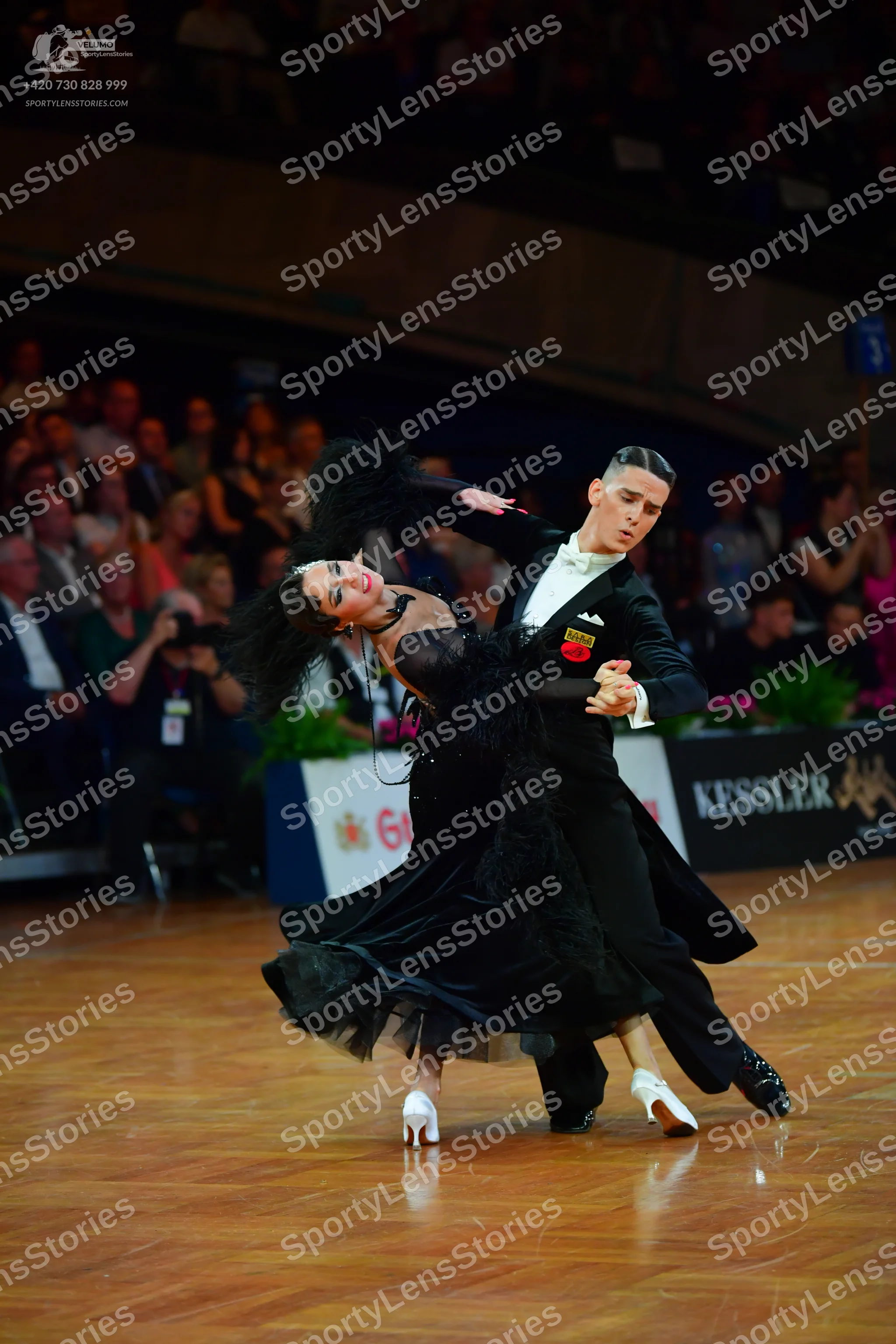 Dancesport competitor: Male dancer: black suit with a white shirt and bowtie, featuring a small red and
