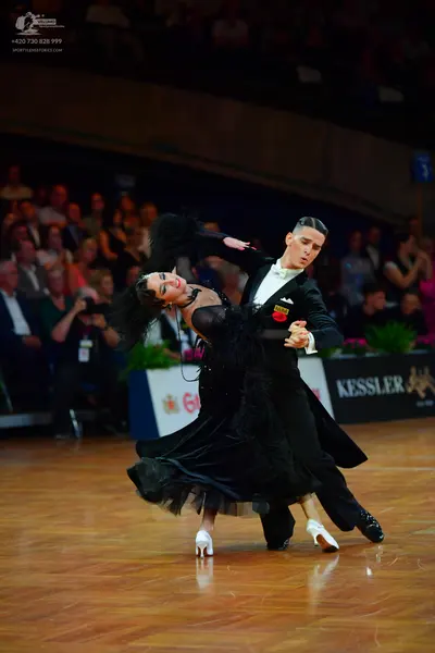 Dancesport competitor: Male dancer: black suit with a white shirt and bowtie, featuring a small red and