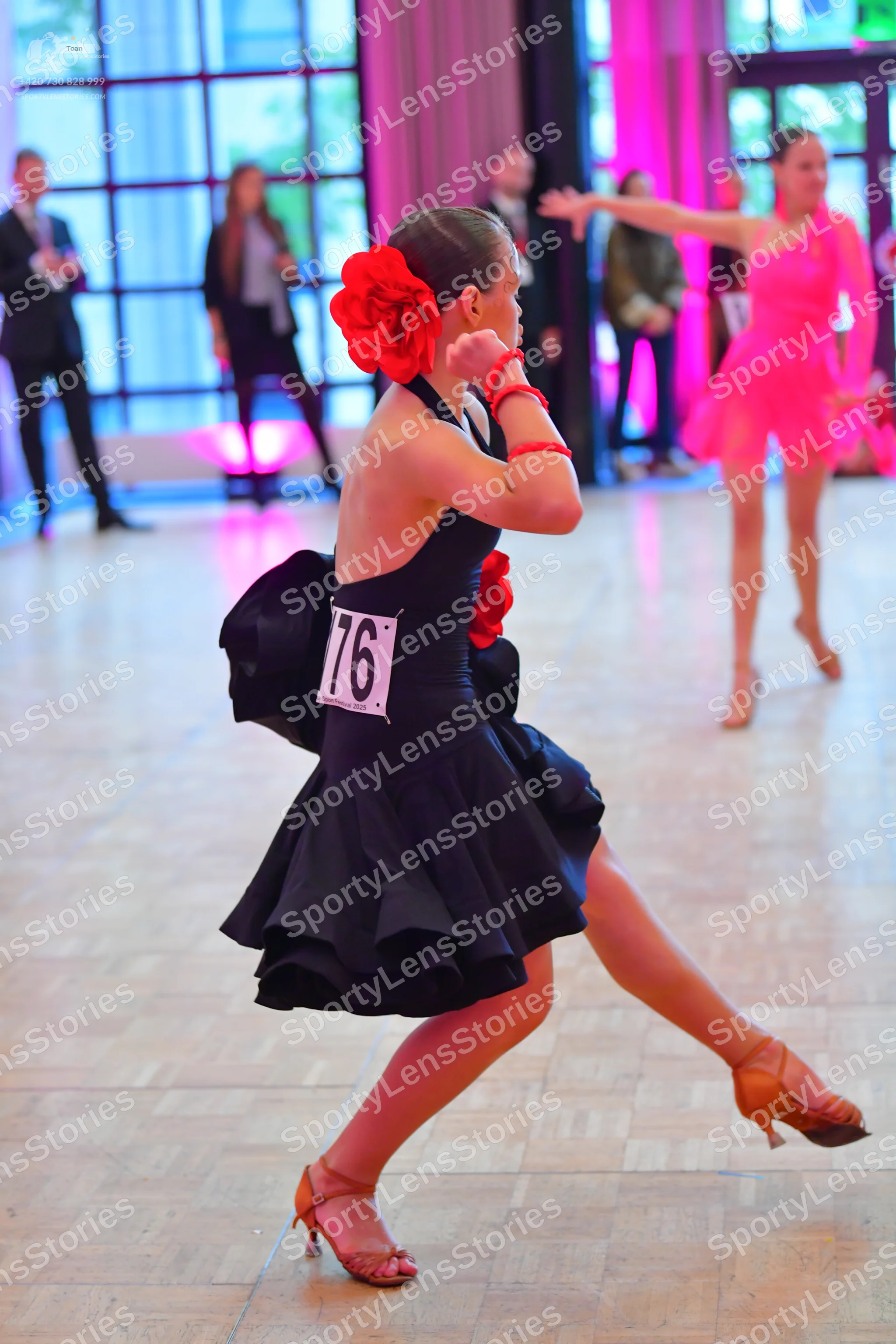 Dancesport competitor #76: Female dancer in foreground: black latin dress with a ruffled skirt, red floral