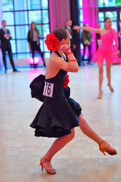 Dancesport competitor #76: Female dancer in foreground: black latin dress with a ruffled skirt, red floral 