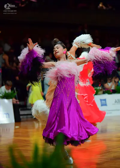 Dancesport competitor: Female dancer 1: Purple satin Latin dress featuring voluminous white, pink, and 