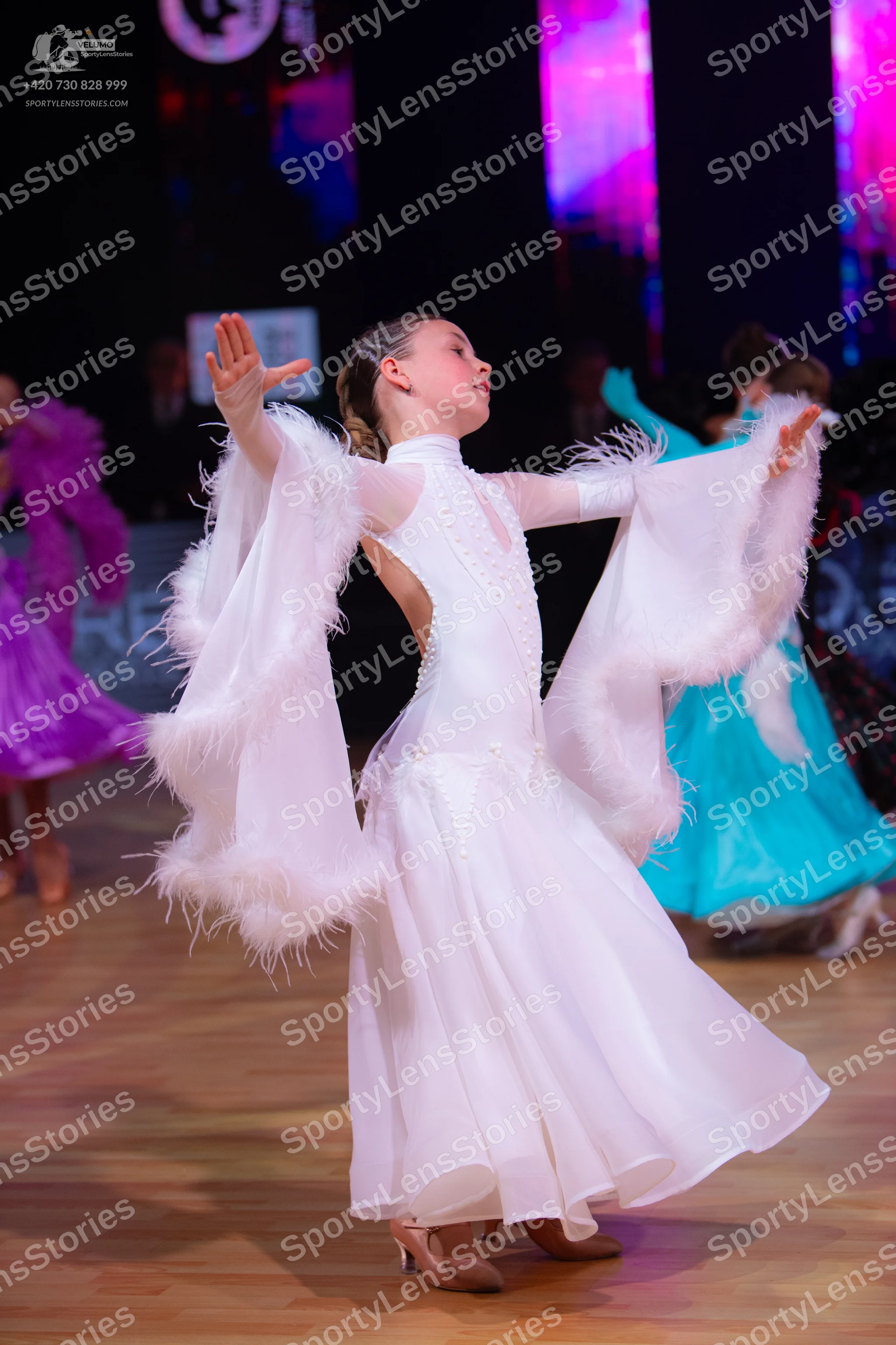 Dancesport competitor: Female dancer in foreground: long white ballroom dress with large, flowing sleev