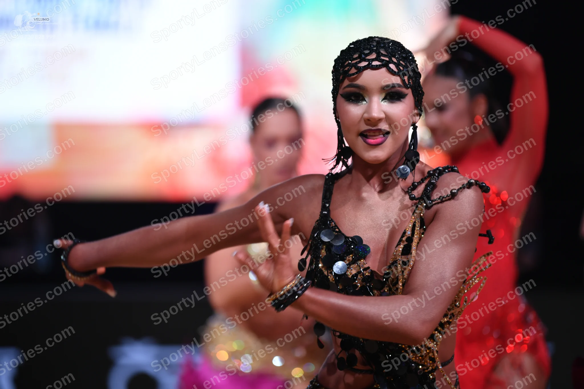 Dancesport competitor: Foreground dancer: black Latin-style costume with heavy black and gold sequin an