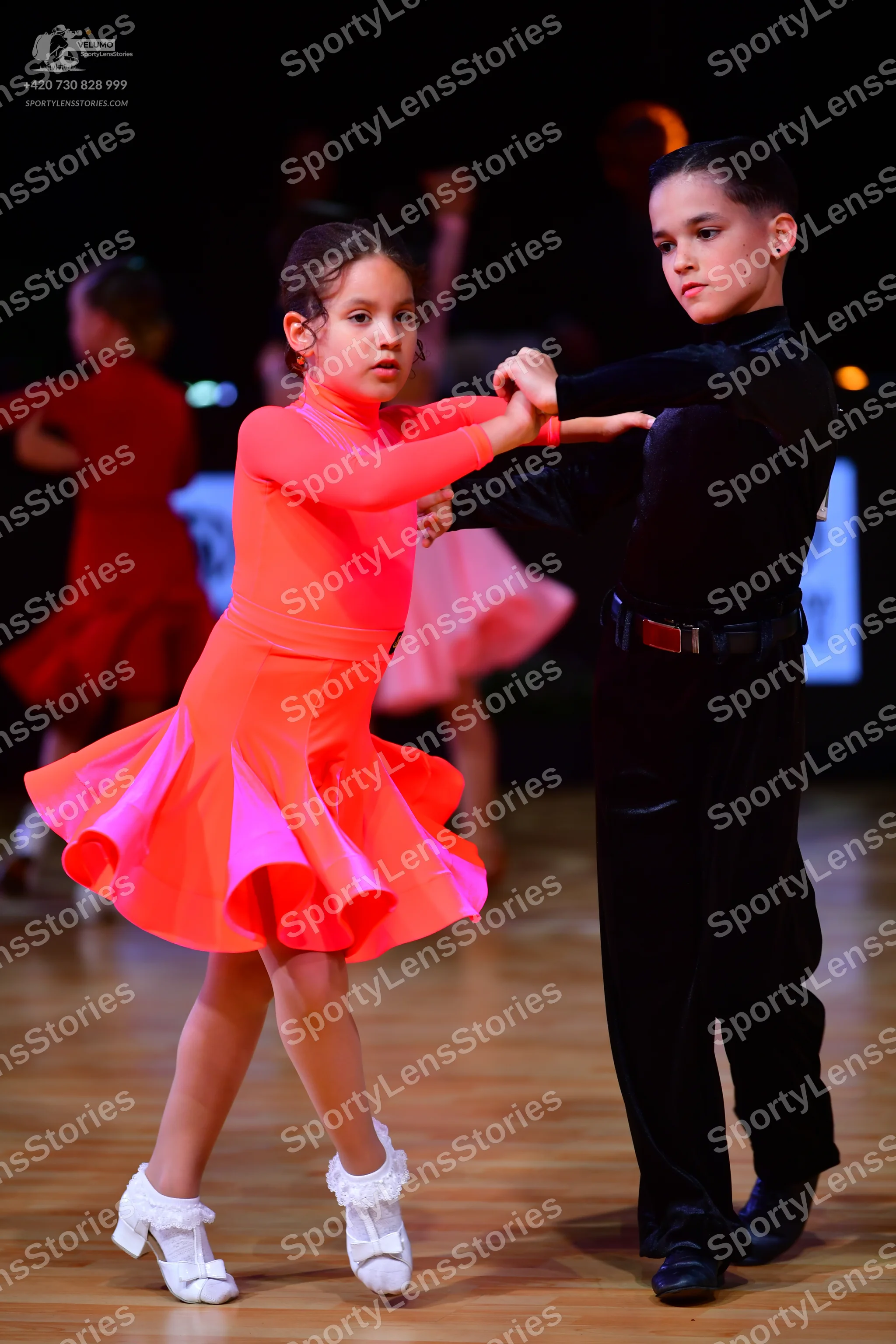 Dancesport competitor: Female dancer: neon pink/orange long-sleeved latin dress with a ruffled skirt an