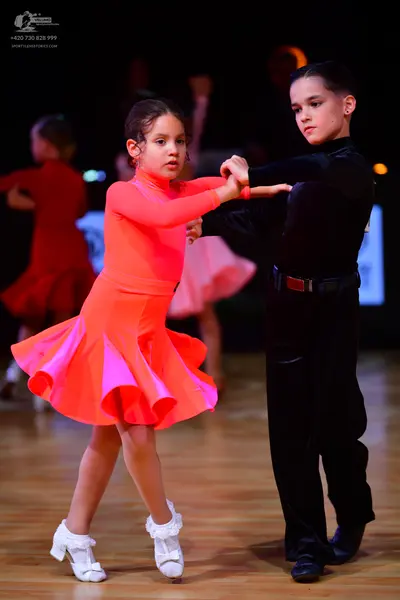 Dancesport competitor: Female dancer: neon pink/orange long-sleeved latin dress with a ruffled skirt an