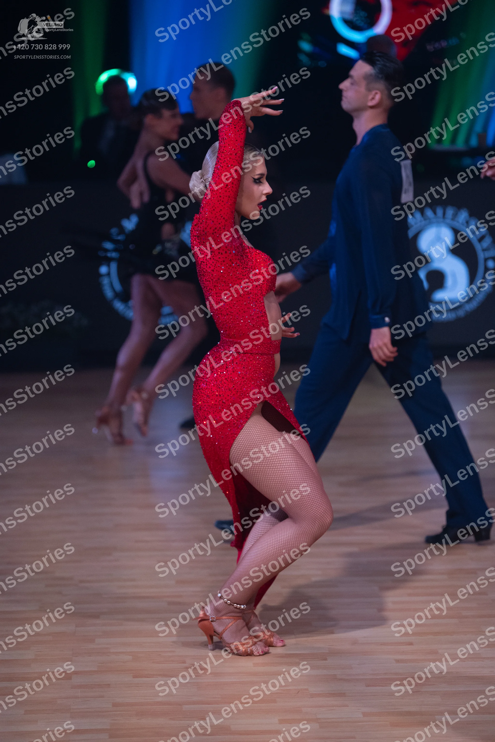 Dancesport competitor: Female dancer in center: red long-sleeved Latin dress with sequins and a high sl